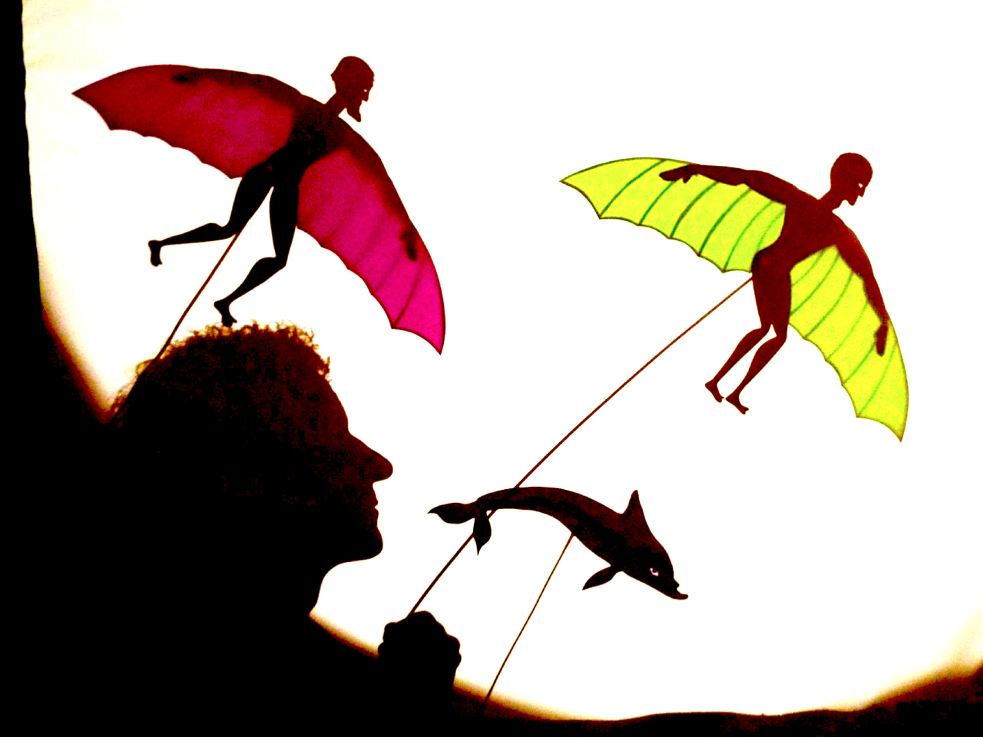 Winged Icarus shadow puppets and a dolphin flying above a silhouetted profile