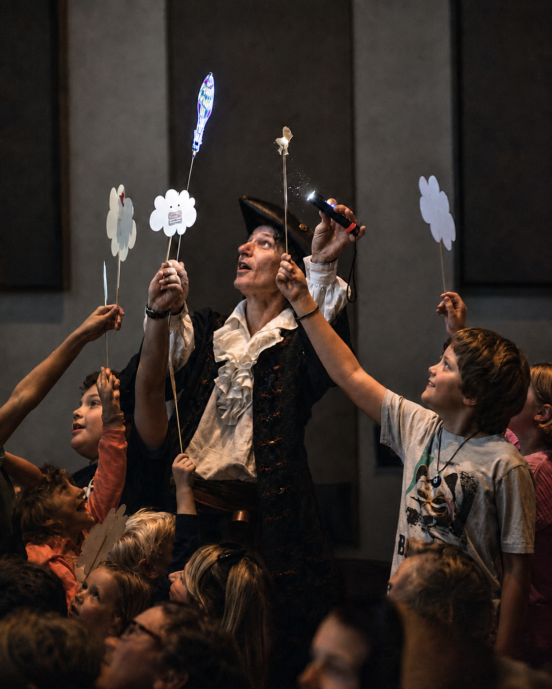 Children holding lit cloud puppets in the air with Mr. Damon during a performance