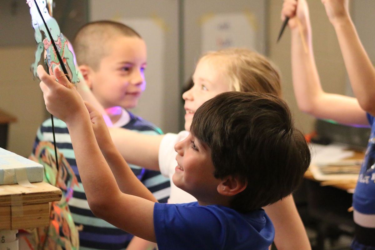 Children raising shadow puppets on rods during a workshop