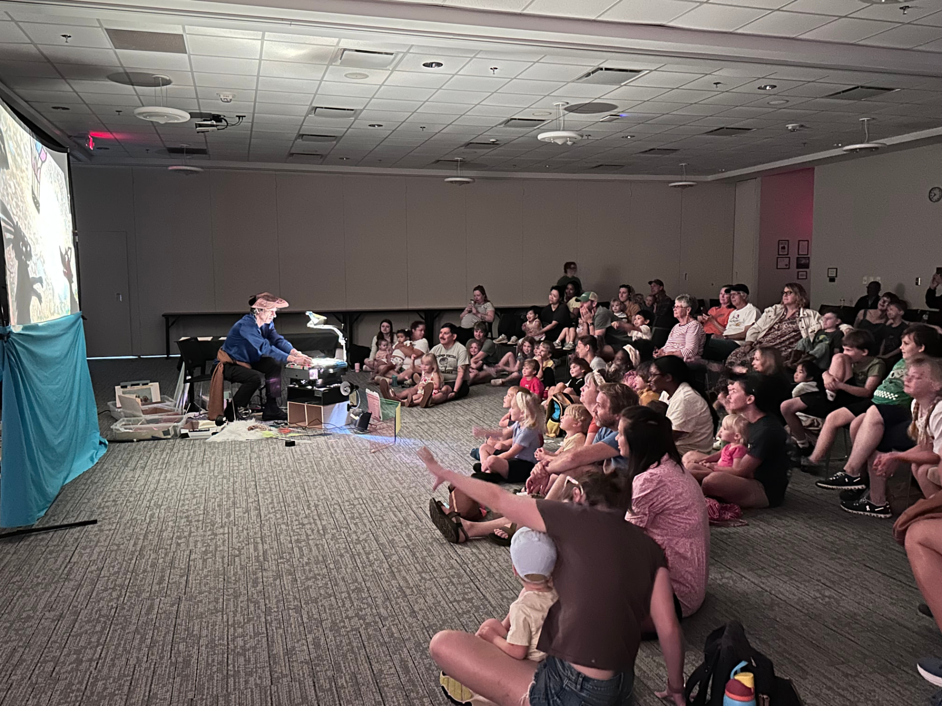 A full family audience seated for a Mr. Damon shadow puppet show