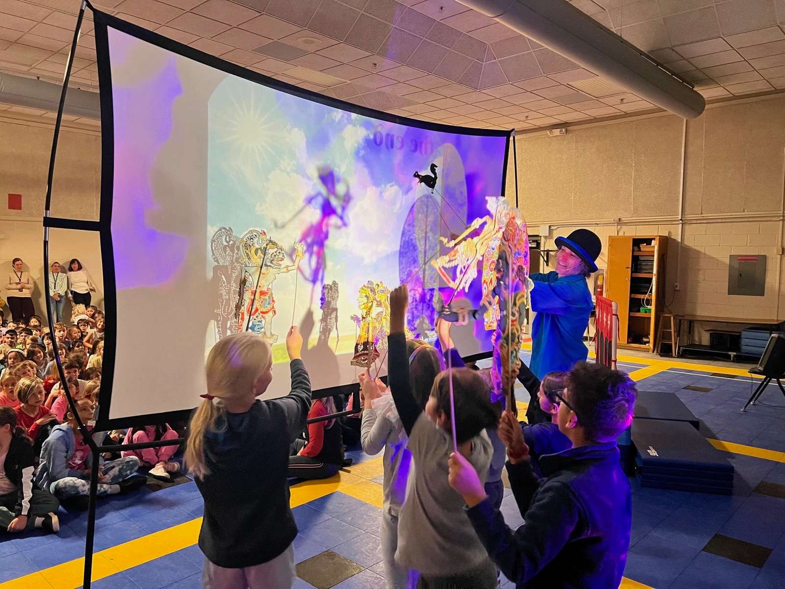 Students holding colorful Asian rod puppets at a lit shadow screen